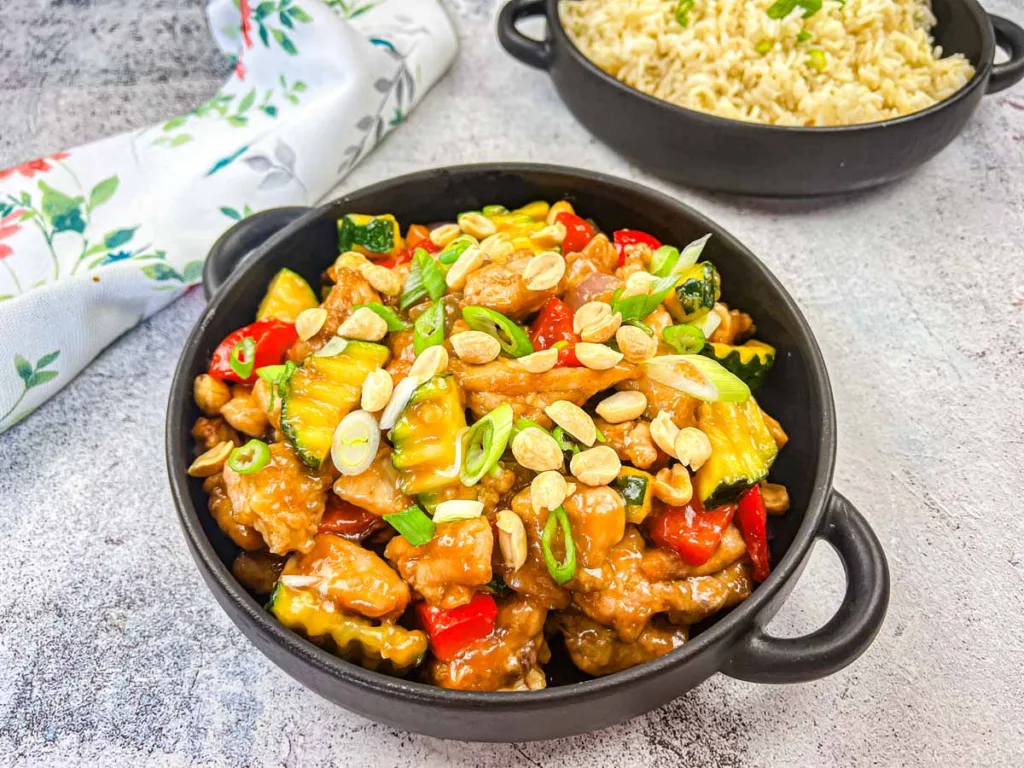 Kung Pao Chicken in a bowl with a bowl of rice in the background.