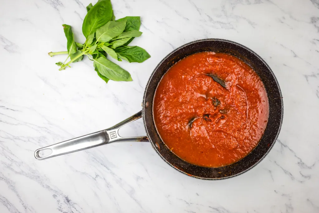 Cooked tomato paste beside basil.