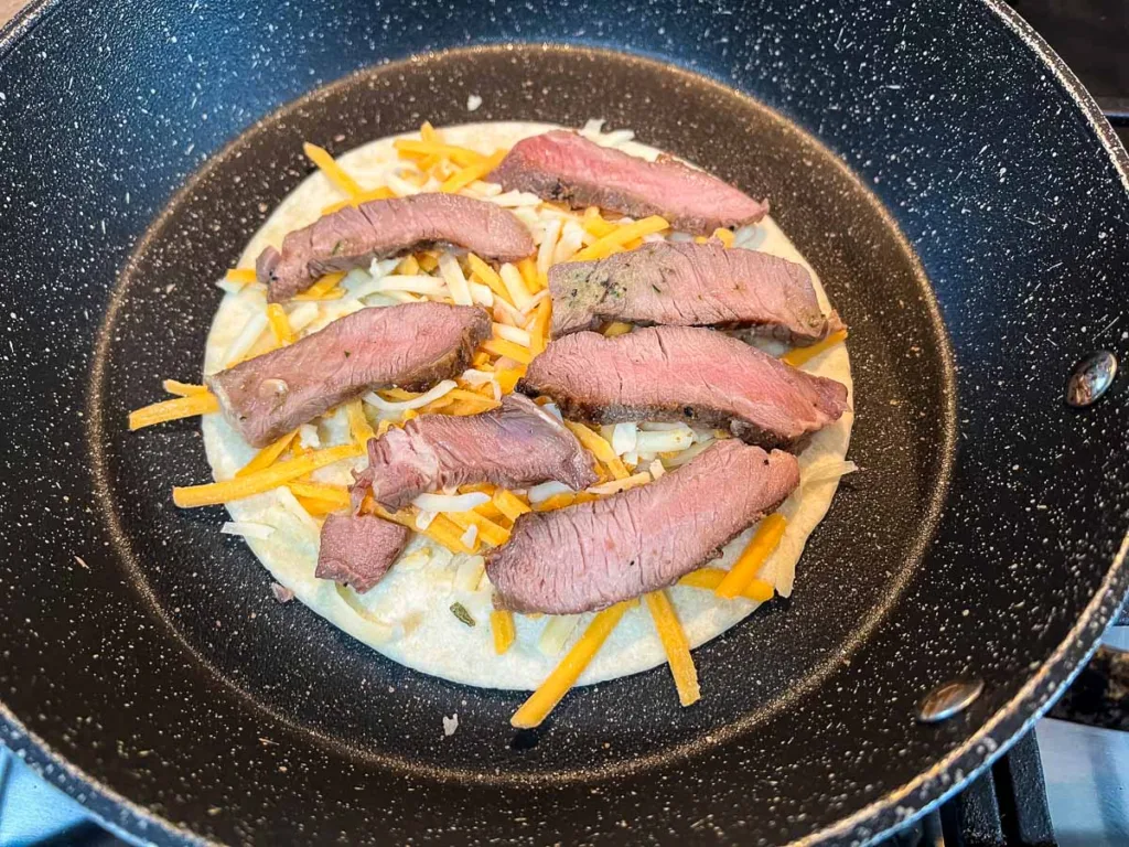 Cheese and steak on a tortilla in a skillet.