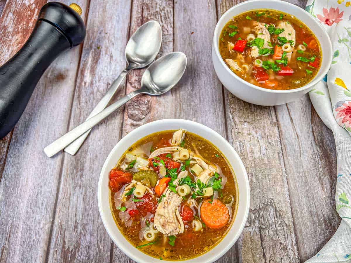 Two bowls of Copycat Carrabba's Mama Mandola's Chicken Soup and two spoons on a table.