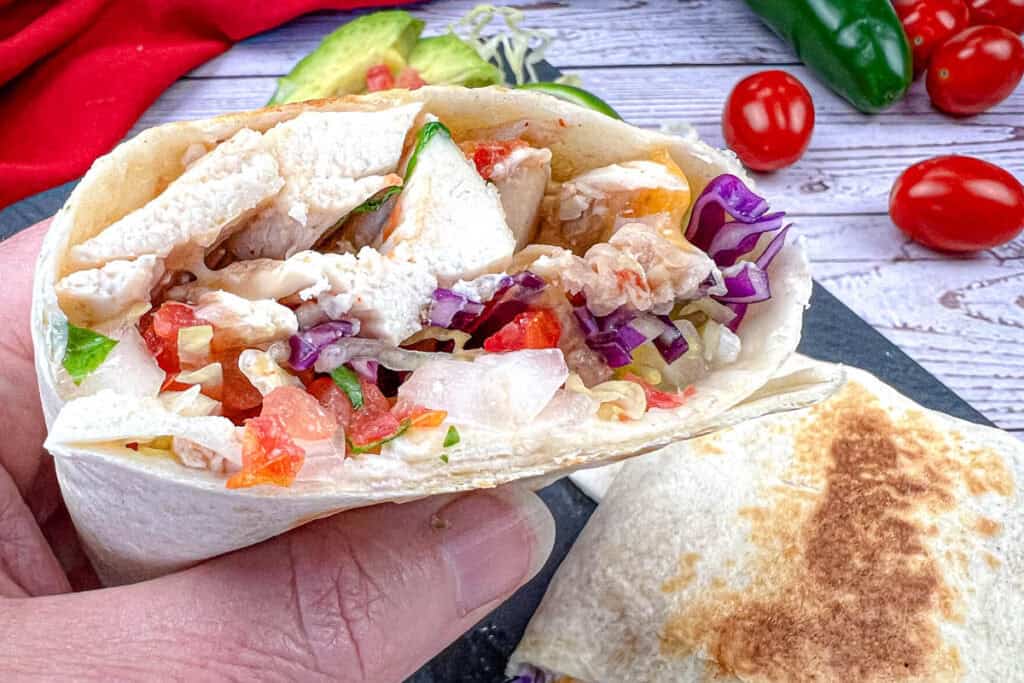 A close-up of a hand holding a copycat Taco Bell Cantina chicken burrito.