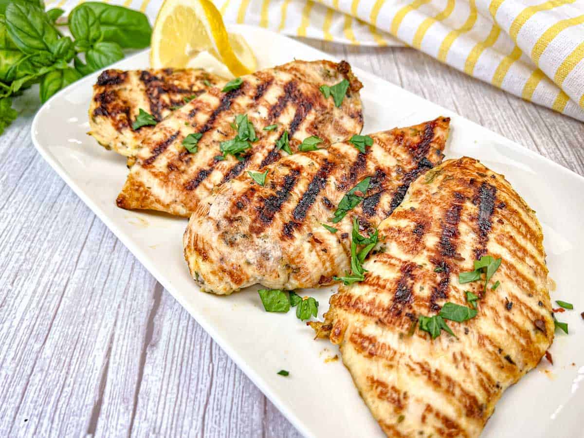 Four pieces of Ninja Woodfire Grill Lemon-Herb Chicken served on a white rectangular plate.