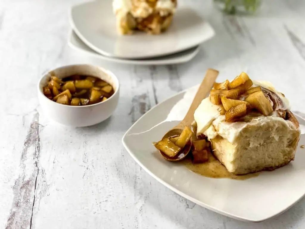 An apple cinnamon roll on a plate with a spoon.