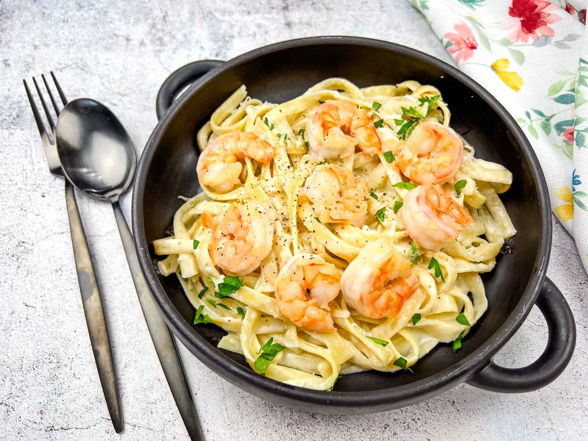 A bowl of olive garden creamy shrimp alfredo pasta served in a black bowl with a spoon.