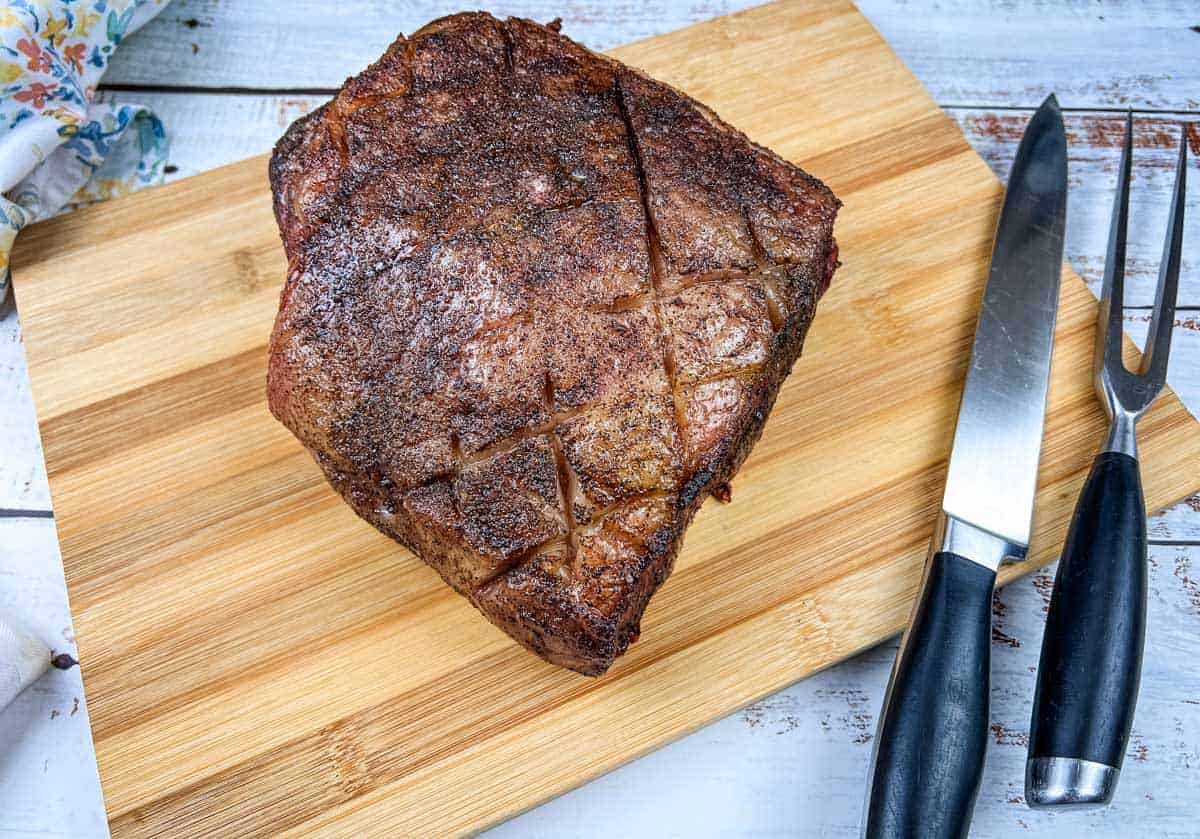 A piece of smoked New York strip roast meat on a cutting board next to a knife.