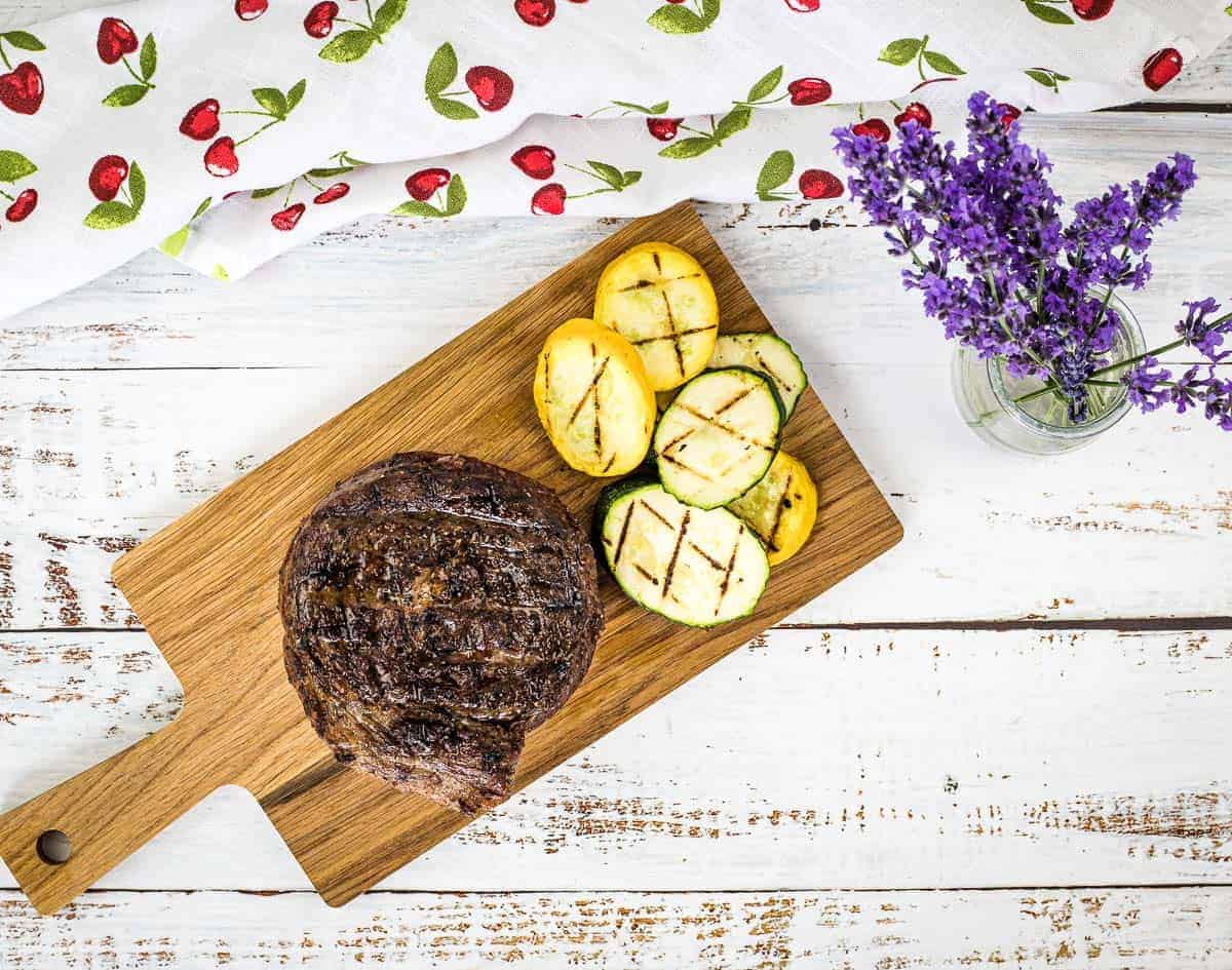 A top-down shot of Grilled Ribeye Cap Steak on a cutting board with veggies.