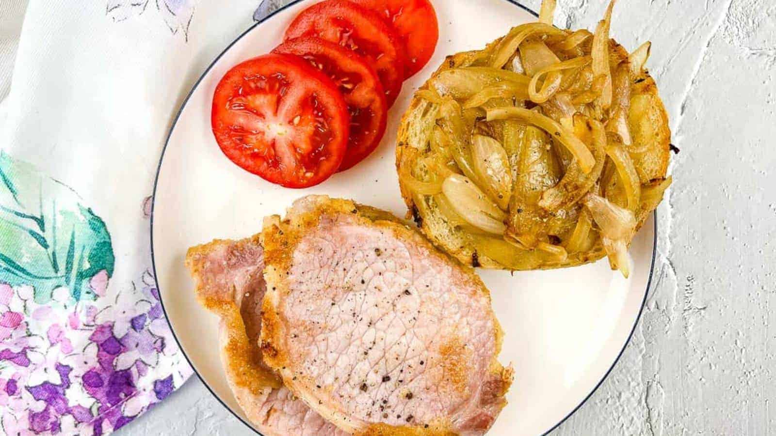 Peameal bacon on a plate with tomatoes and onions.