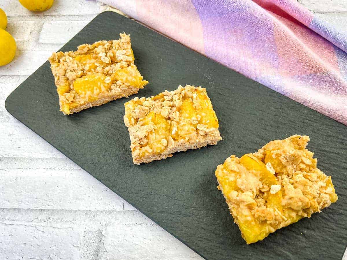 Yellow plum crumb bars on a black slate.