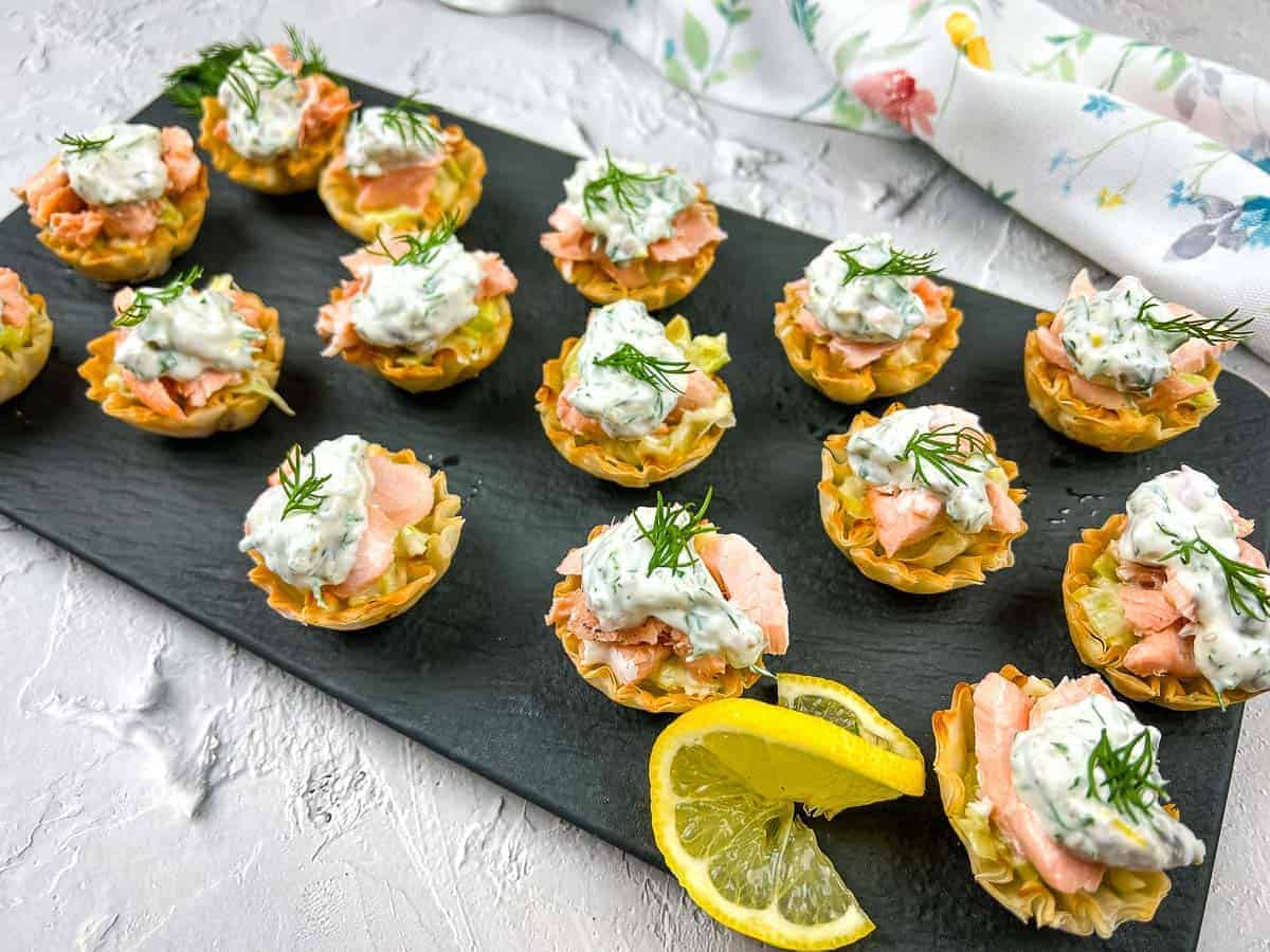 Salmon & Leek Phyllo Tartlets with lemon wedges on a black plate.