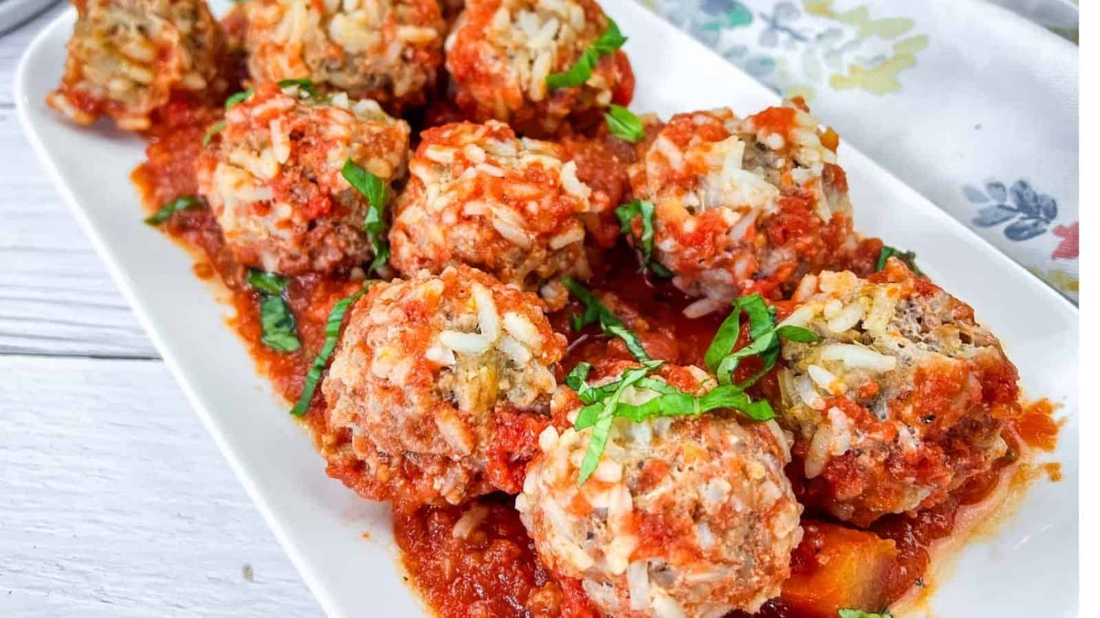 A white rectangular plate with several meatballs covered in tomato sauce, garnished with chopped basil.