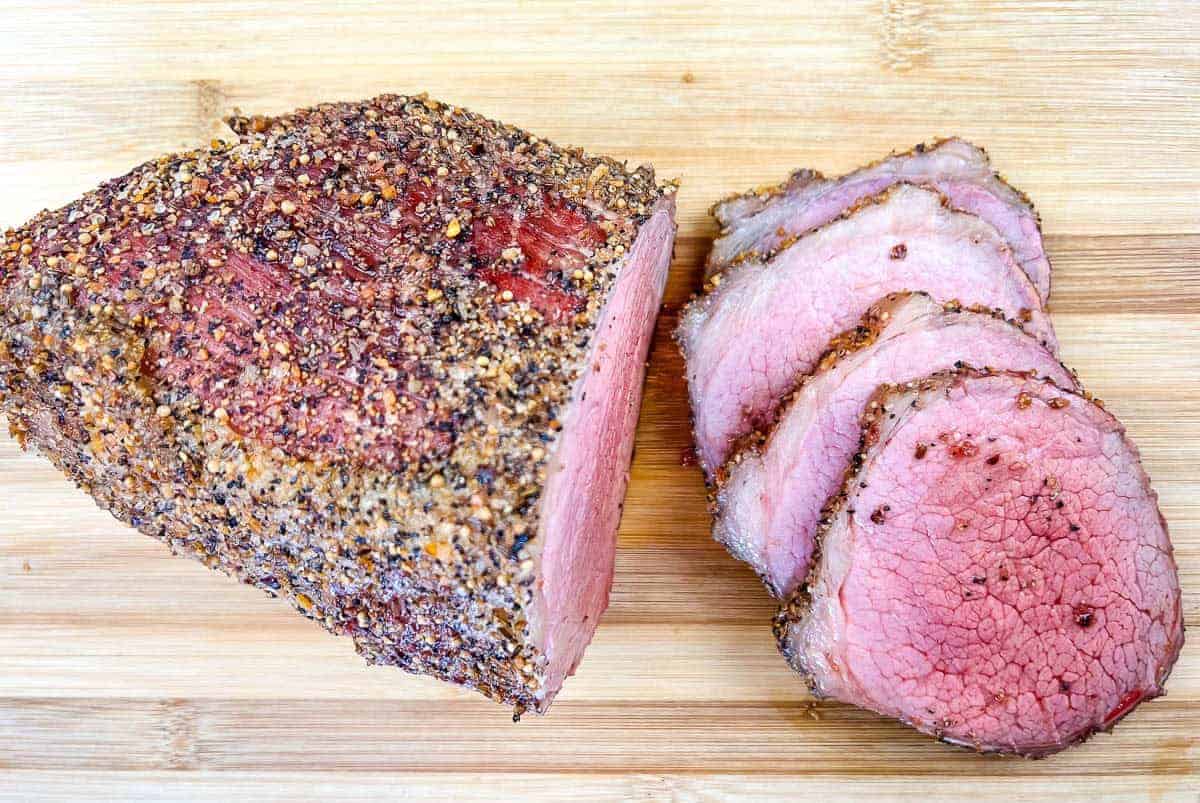 A whole and sliced smoked eye of round with on a wooden cutting board.