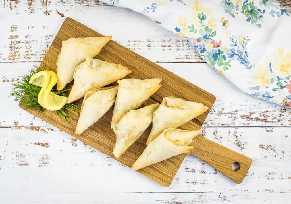 Crab Spanakopita triangles on a cutting board.