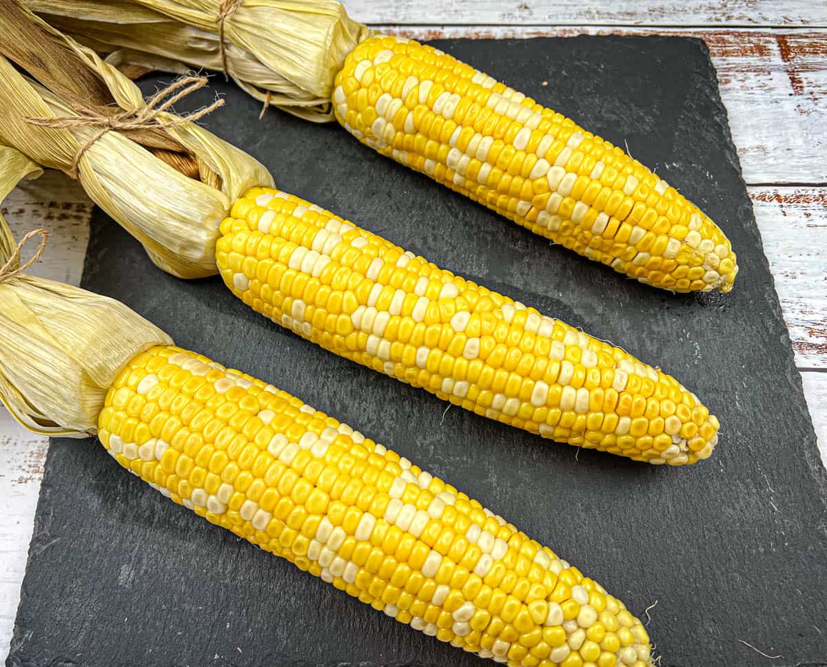 Three ears of husked corn were arranged on a dark slate plate.