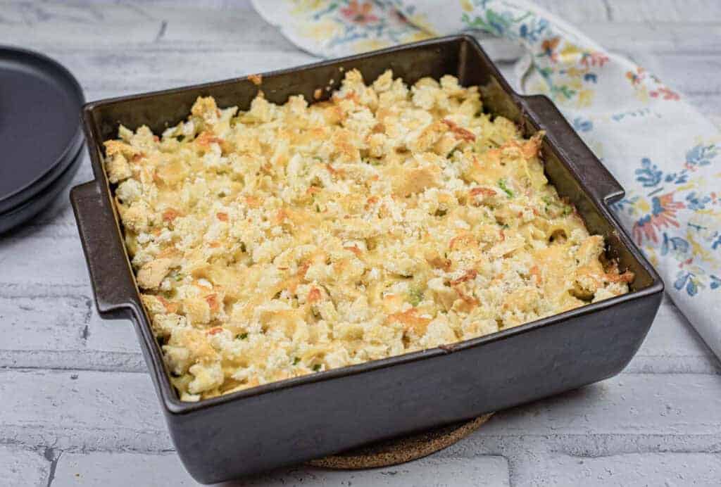 Top-down shot of Tuna Noodle Casserole on a dish with a small portion on a black plate.