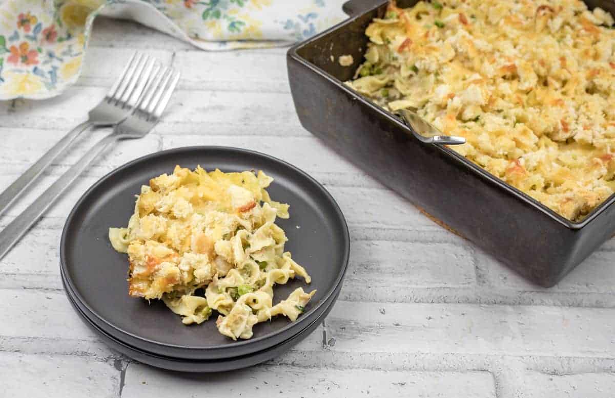 Top-down shot of Tuna Noodle Casserole on a dish with a small portion on a black plate.