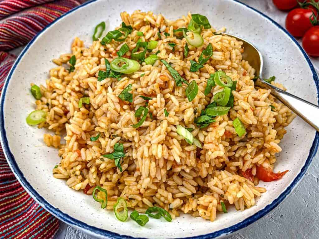 A plate of Mexican rice garnished with chopped green onions and herbs served with a spoon.