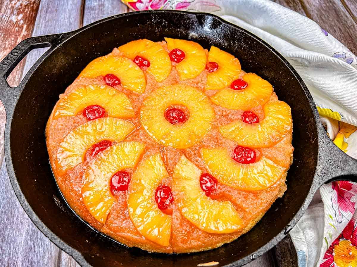 A pineapple upside-down cake with cherry toppings in a cast iron skillet.