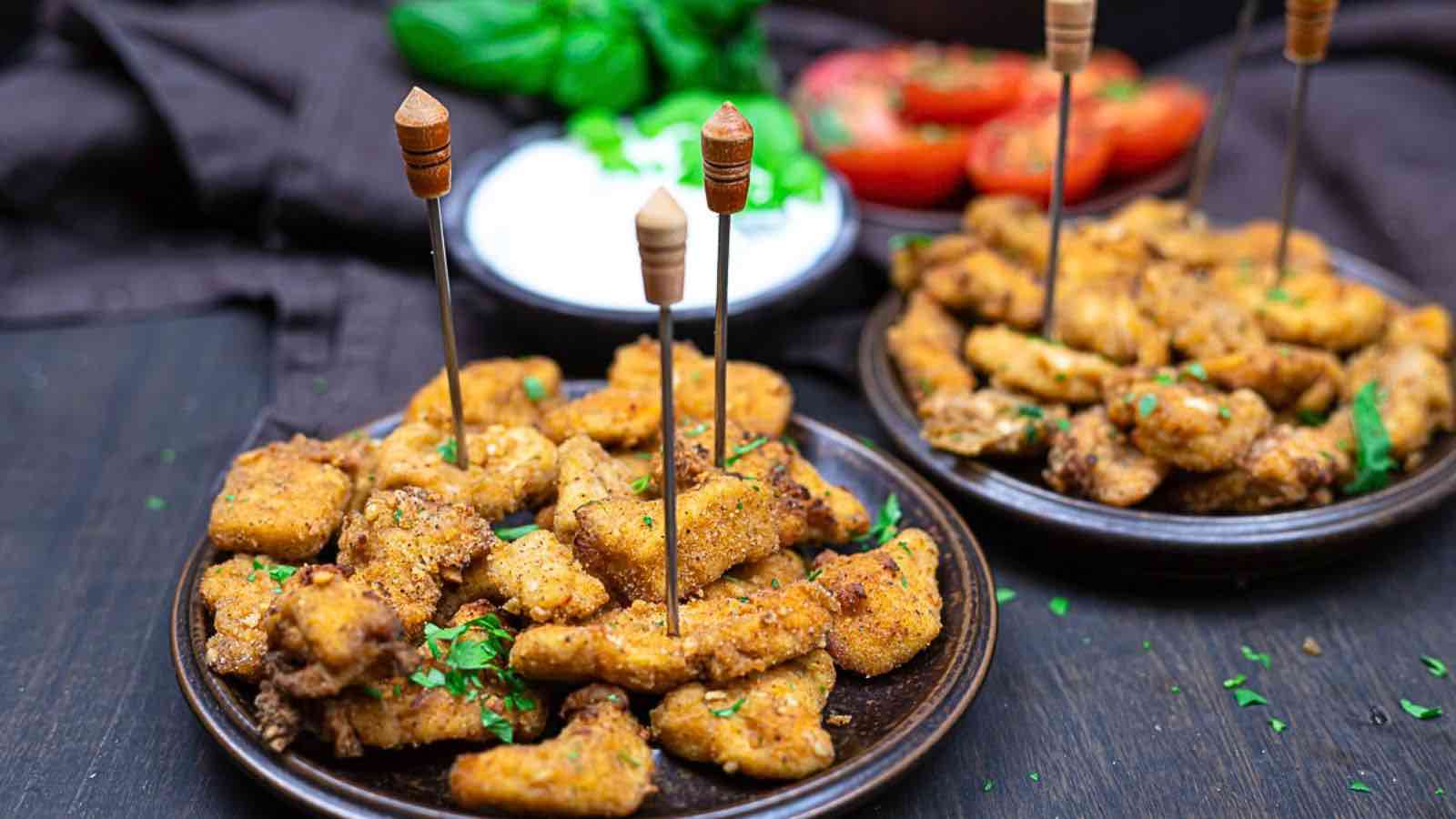 Plates of breaded and fried chicken nuggets with skewers, garnished with herbs.