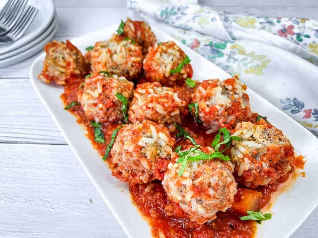 A white rectangular plate with several meatballs covered in tomato sauce, garnished with chopped basil.