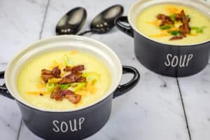 Two bowls of Copycat La Madeleine Country Potato Soup were placed on a marble surface next to two spoons.