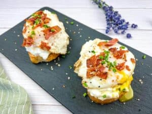 A slate platter with two slices of Cottage Cheese Toast with Bacon & Poached Egg.