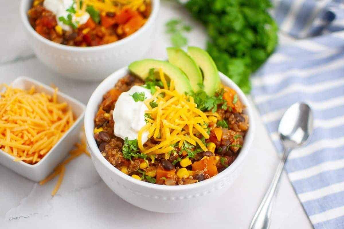 Two bowls of quinoa salad topped with avocado slices, cheese, and sour cream.