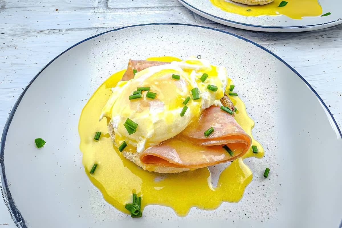 Eggs Benedict with poached eggs, ham, and hollandaise sauce on a plate, garnished with chives.