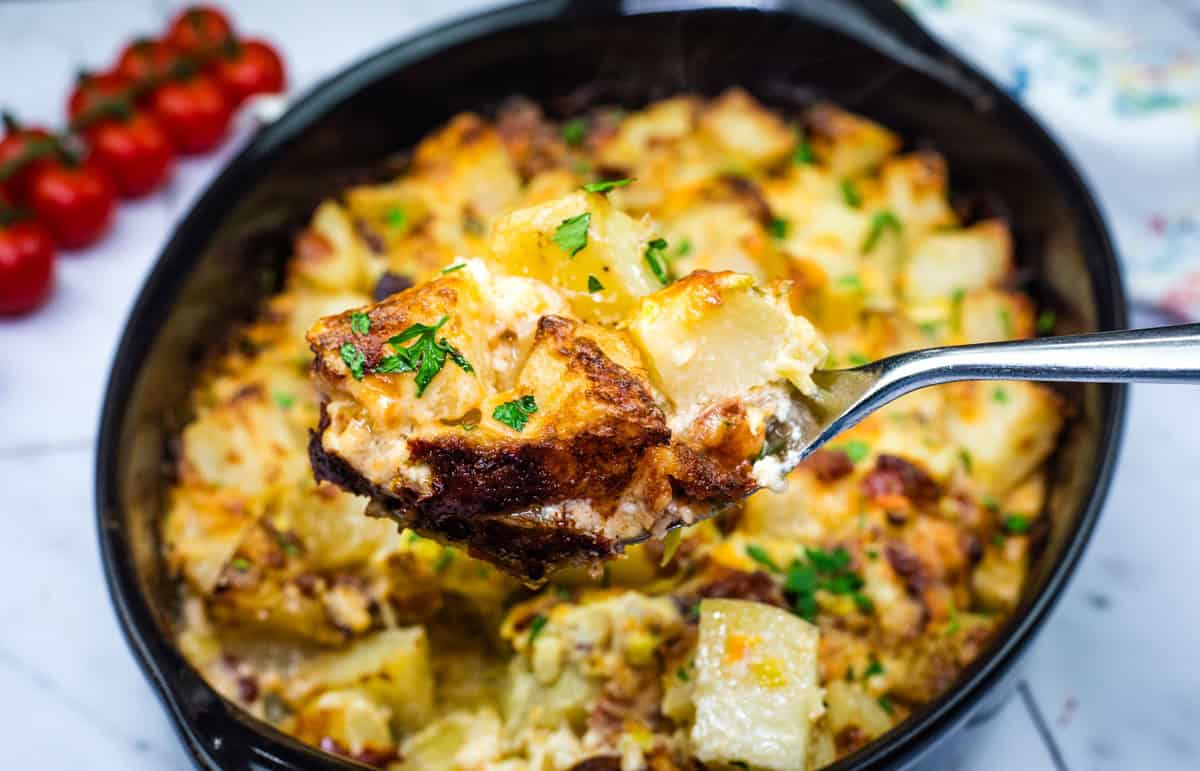 A spoonful of Mississippi Mud Potatoes with herbs, held above a dish.