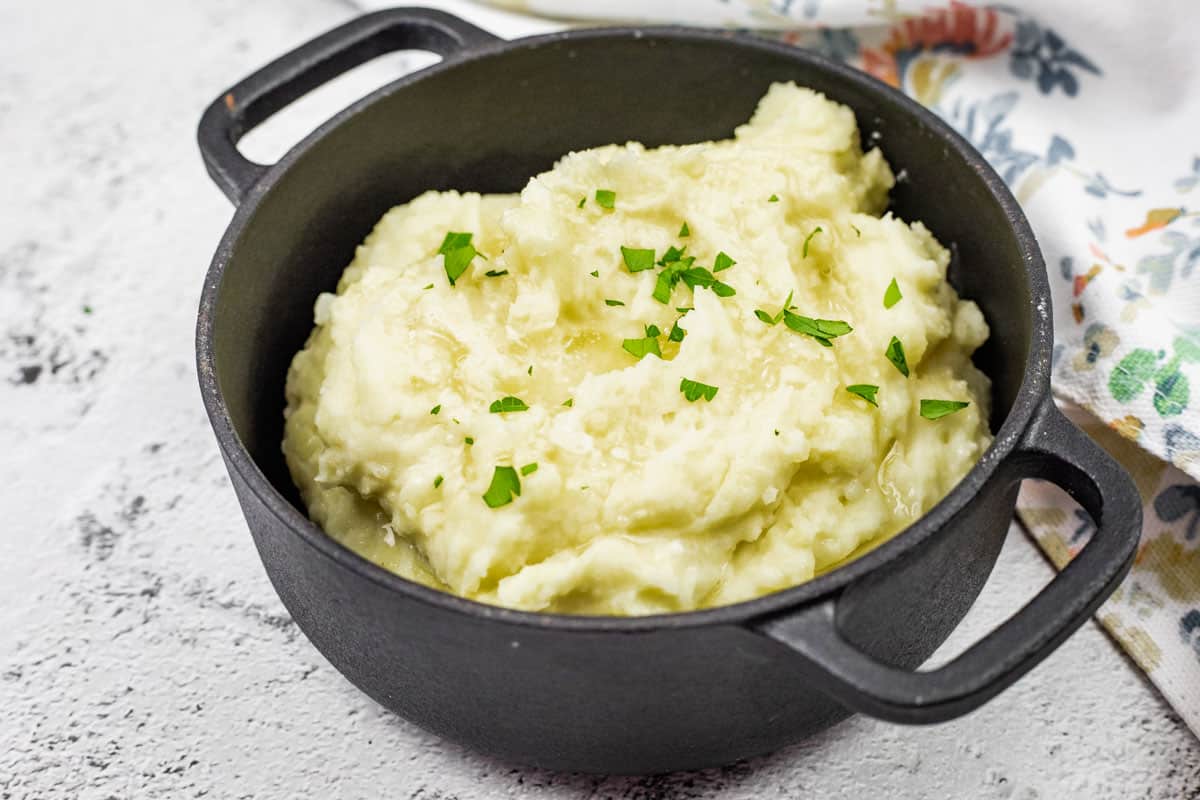 A black pot filled with Creamiest mashed potatoes, topped with chopped parsley.