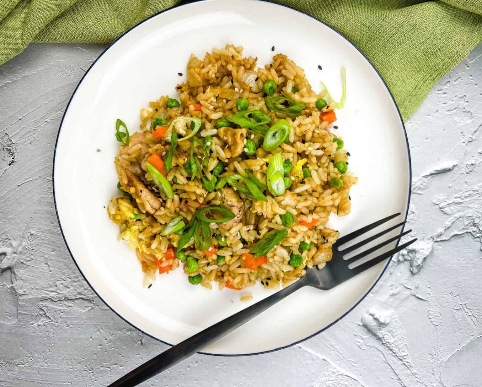 A plate of Turkey fried rice with a fork, set against a green cloth on a textured surface.
