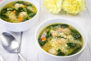 Two bowls of Italian soup accompanied by yellow flowers and a spoon.