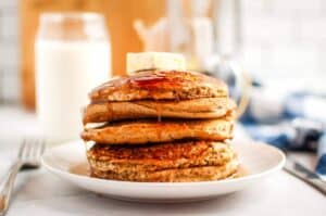 A stack of Buttermilk Oatmeal Pancakes with syrup and a pat of butter on top, served on a white plate.