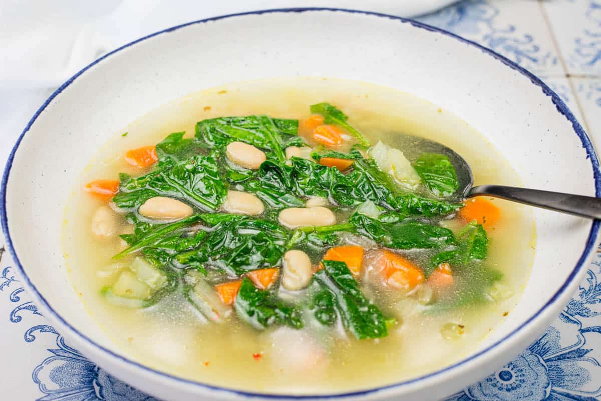 A bowl of rice and white bean soup with served with a spoon on a blue and white patterned surface.