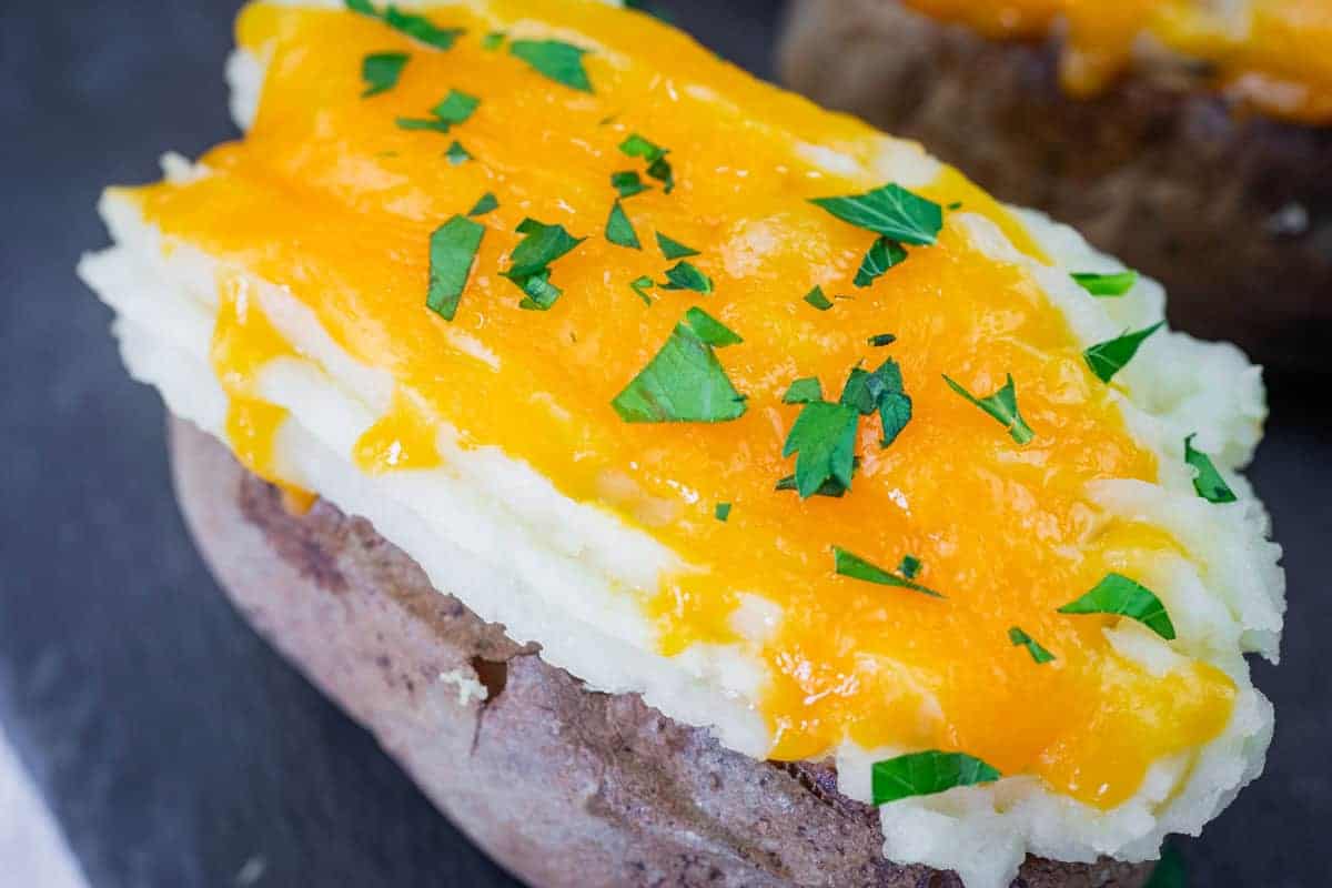 Close-up of Shepherd’s Pie Baked Potatoes topped with melted cheddar cheese and chopped parsley.