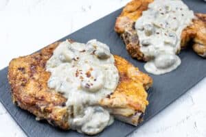 Two Smothered Pork Chops with Onions & Mushrooms on a black rectangular plate.