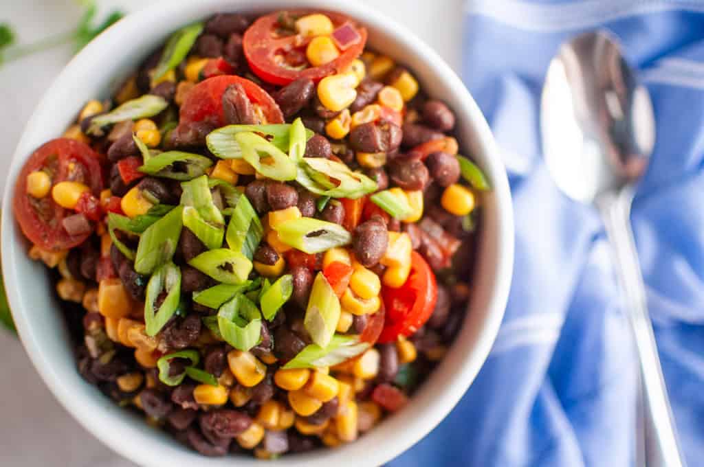 A bowl of black bean and corn salad placed next to a spoon and a blue napkin.