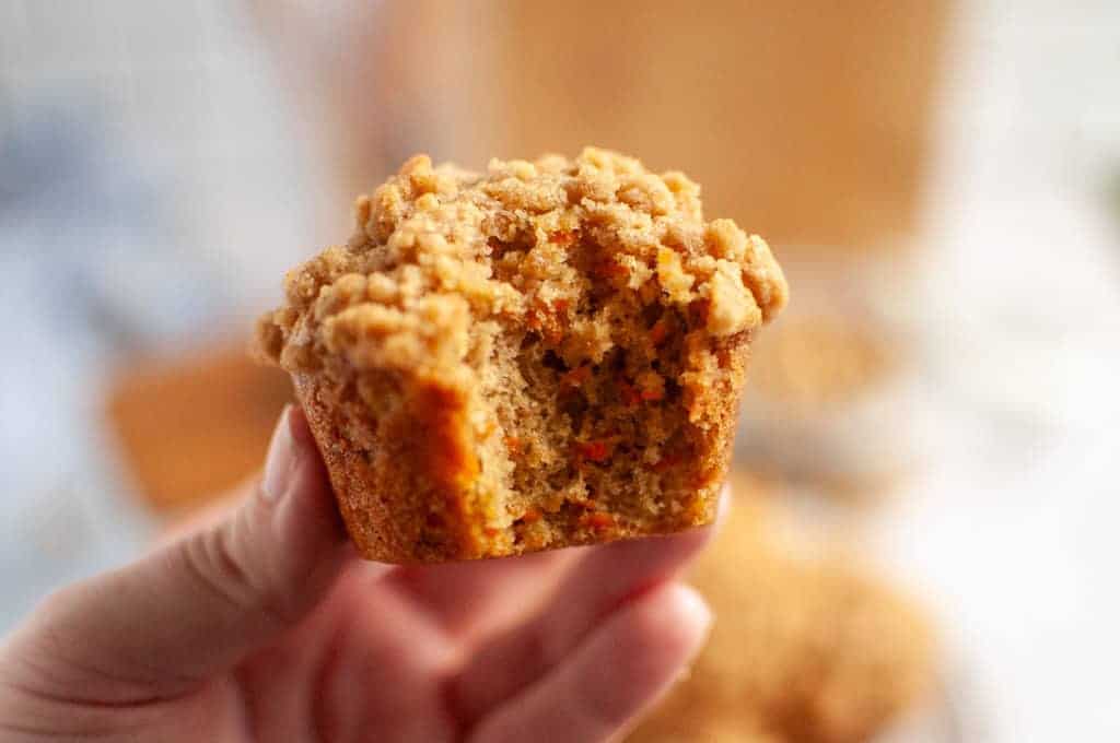 A hand holding a partially eaten Carrot Muffin with Streusel Topping, showing the moist interior.