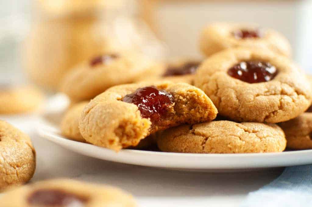 A close-up of peanut butter thumbprint cookies filled with red jelly.