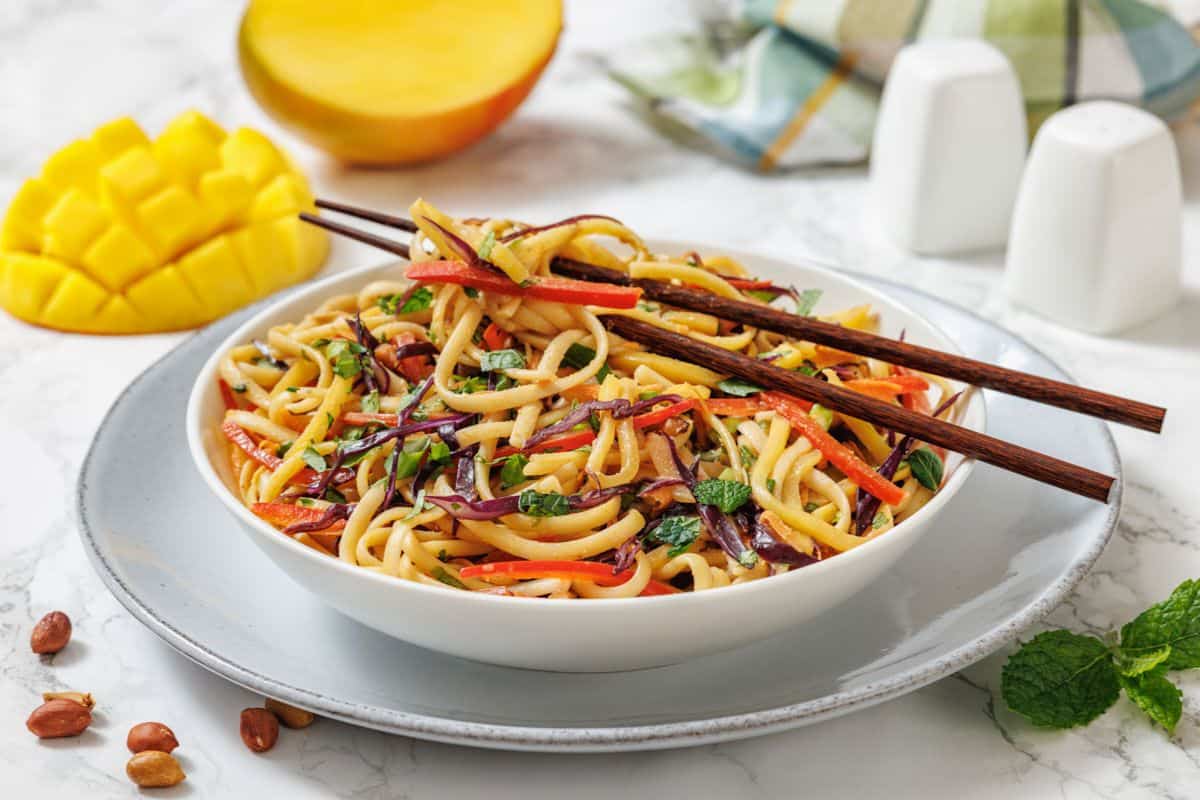 A bowl of noodle salad with mango, garnished with chopsticks.
