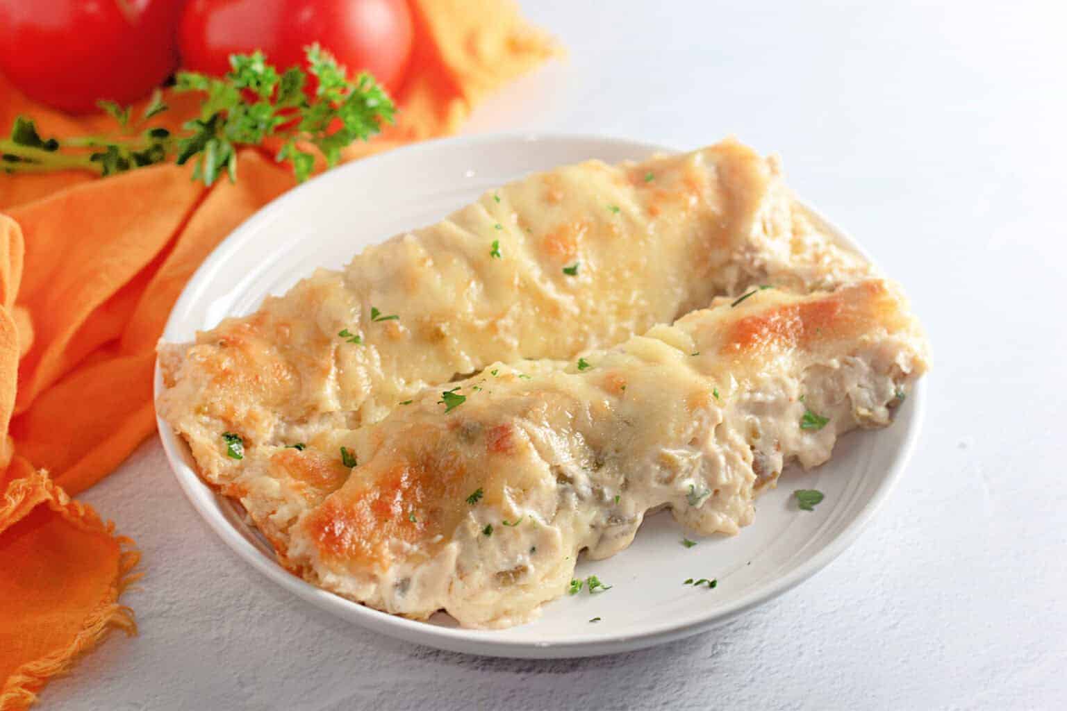 Two White Chicken Enchiladas filled with creamy sauce and topped with melted cheese, served on a white plate with a garnish of chopped parsley.