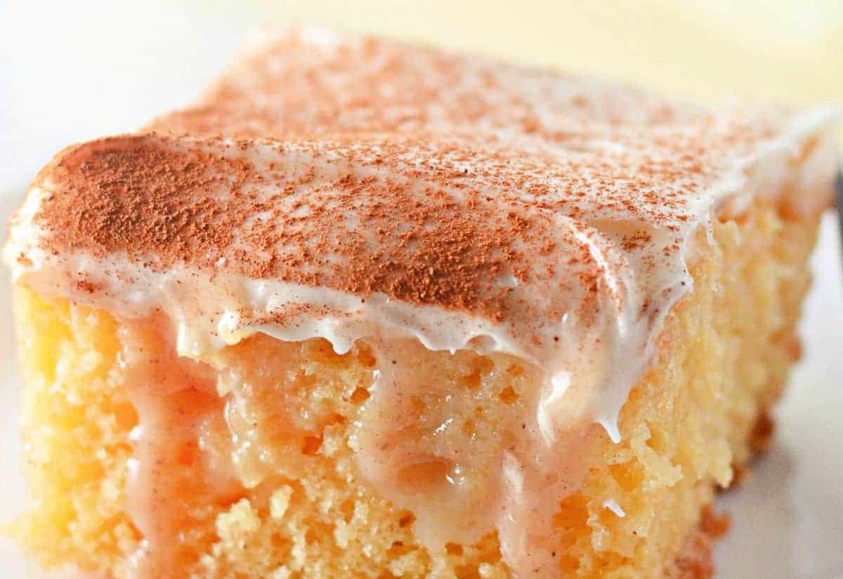 Close-up of a slice of Cinnamon Roll Poke Cake topped with white frosting and sprinkled with cinnamon.