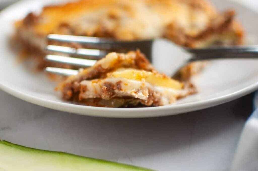 A close-up, slightly high-angle view of Zucchini Lasagna squares arranged on a dark gray baking sheet, each topped with a glossy, light brown apple filling and a generous sprinkle of light brown crumb topping.