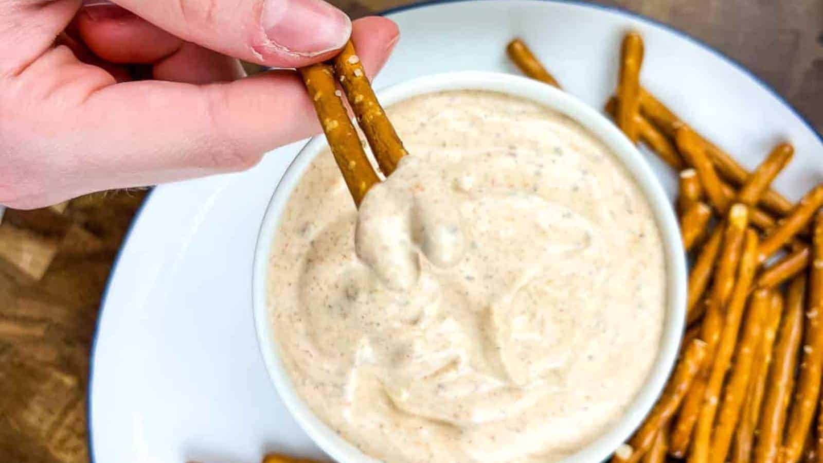 A person dipping a pretzel into a bowl of cajun dip.