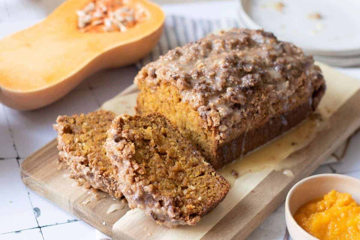 A loaf of Pumpkin Bread with Streusel & Glaze sits on a cutting board, with two slices cut.