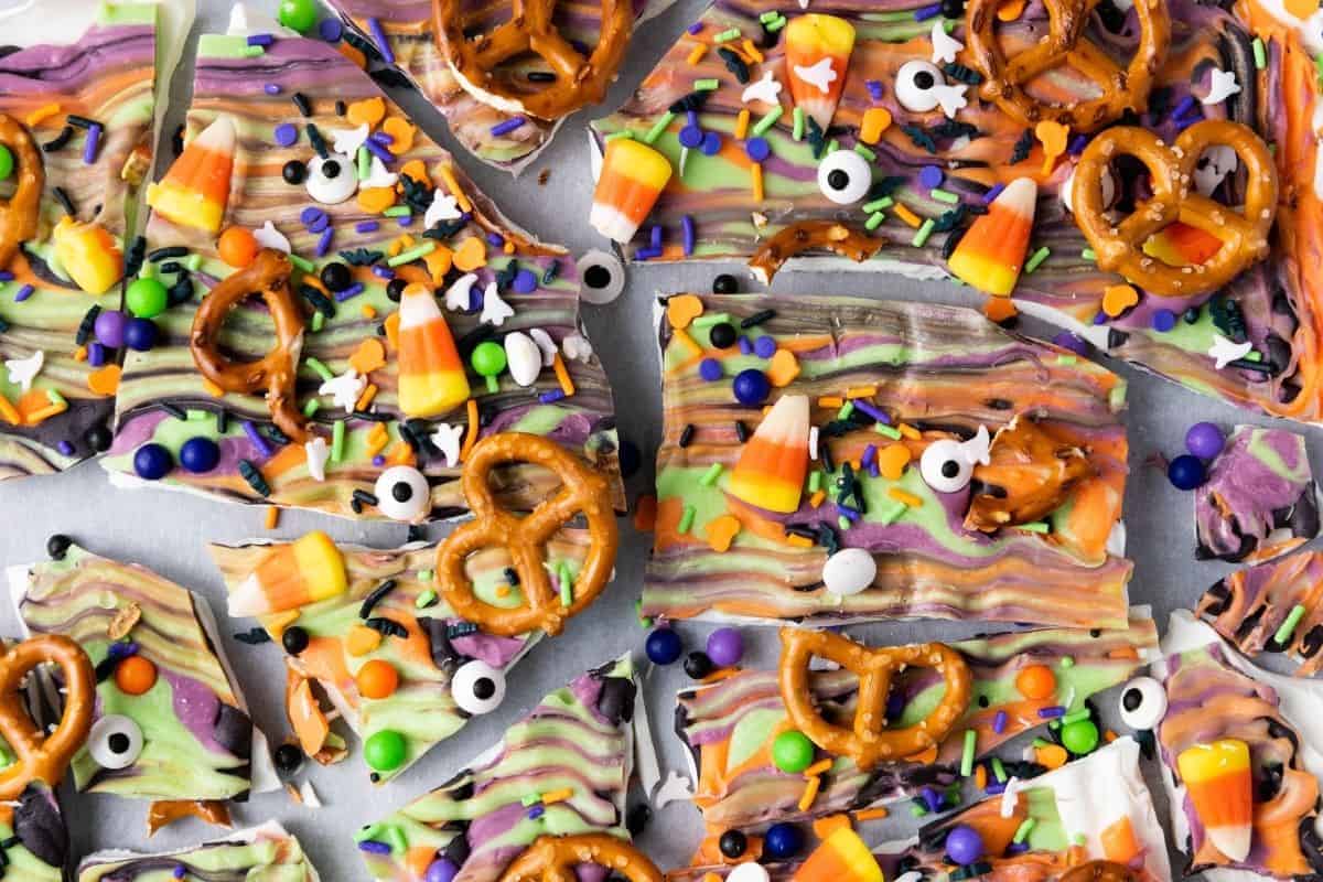 Halloween-themed chocolate bark topped with pretzels, candy corn, candy eyeballs, and colorful sprinkles, broken into irregular pieces.