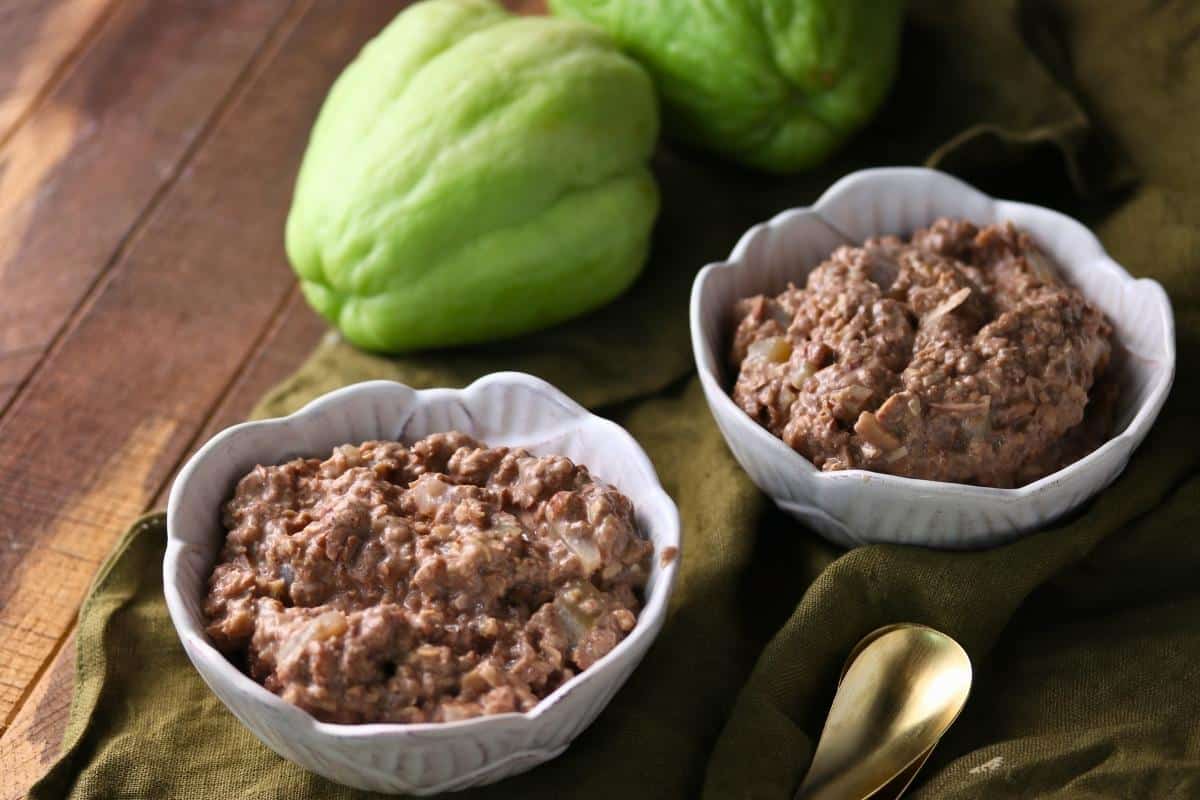 Two cups of Apple Cinnamon Oatmeal with two whole chayote squash and a gold spoon nearby on a wooden surface.