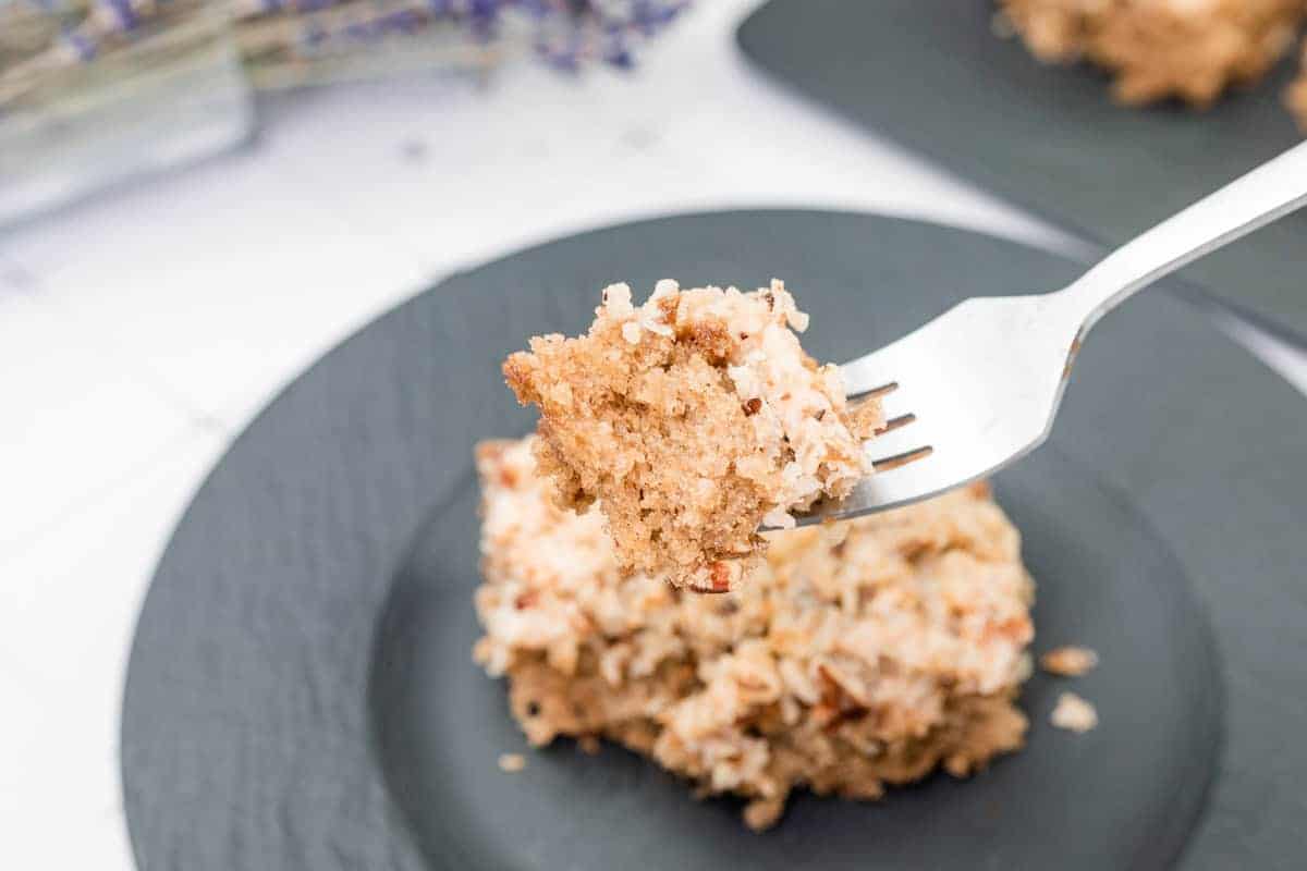 A fork holds a bite of Old Fashioned Oatmeal Cake above a plate with a larger piece of the same cake.