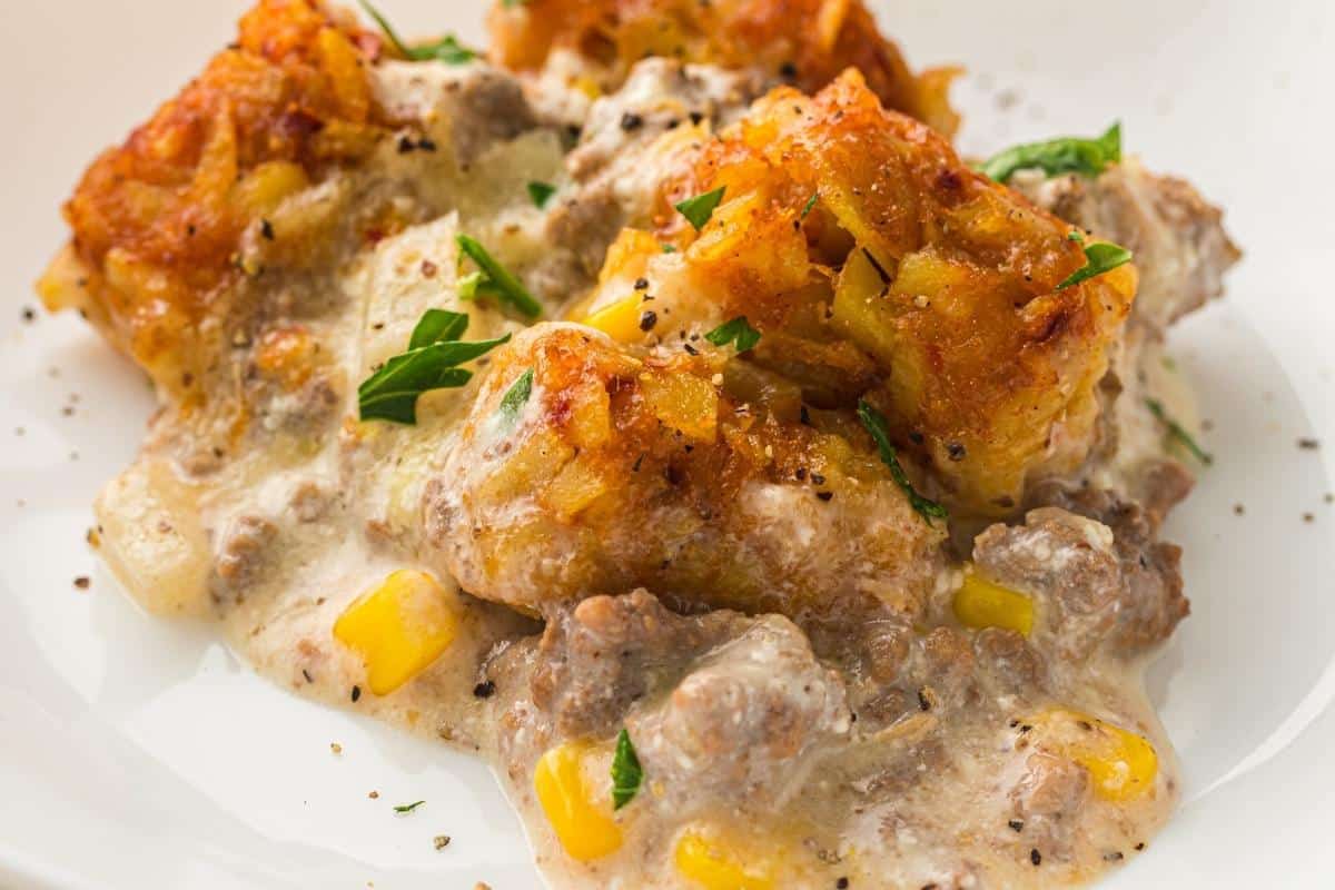 A serving of Slow Cooker Cowboy Casserole topped with crispy tater tots and black pepper on a white plate.