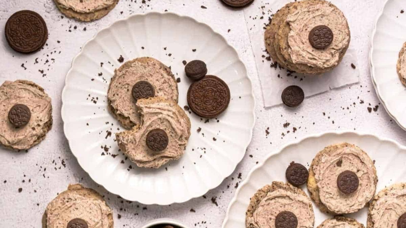 Copycat Crumbl Cookies and Cream Milkshake Cookies arranged on white plates and a light surface with cookie crumbs scattered around.